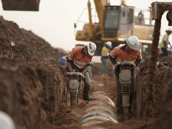 Workers in high-visibility gear laying pipe in an open trench.